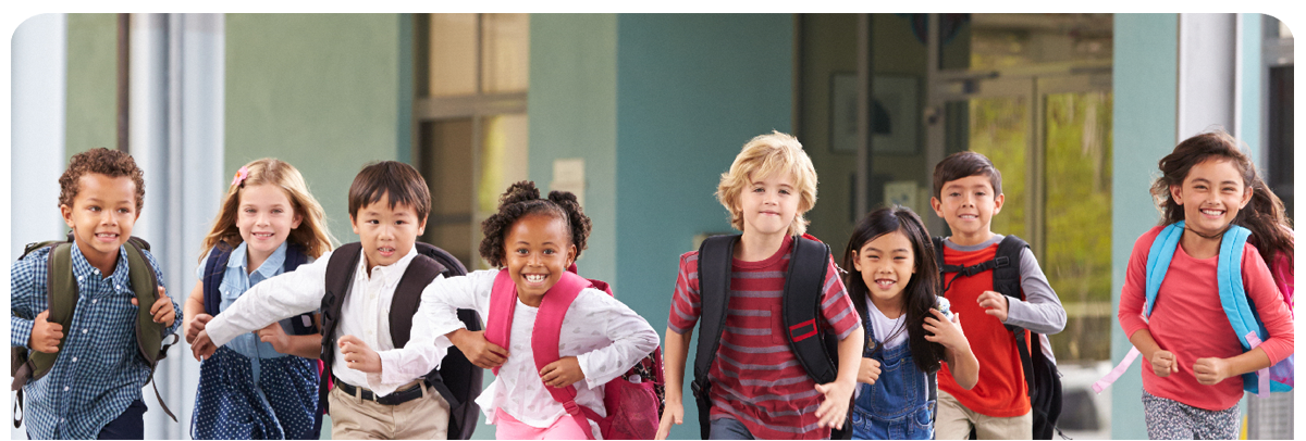 Eight students wearing backpacks run on school grounds