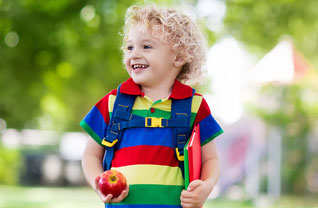 Smiling student stands outside holding an apple and books