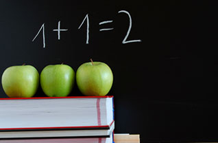 Three apples sit on top of books and 1+1=2 written on a blackboard